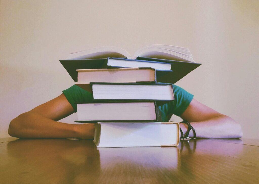 Stack of books on a person's head, representing stress and mental health. Seek therapy for burnout and chronic stress in NYC.